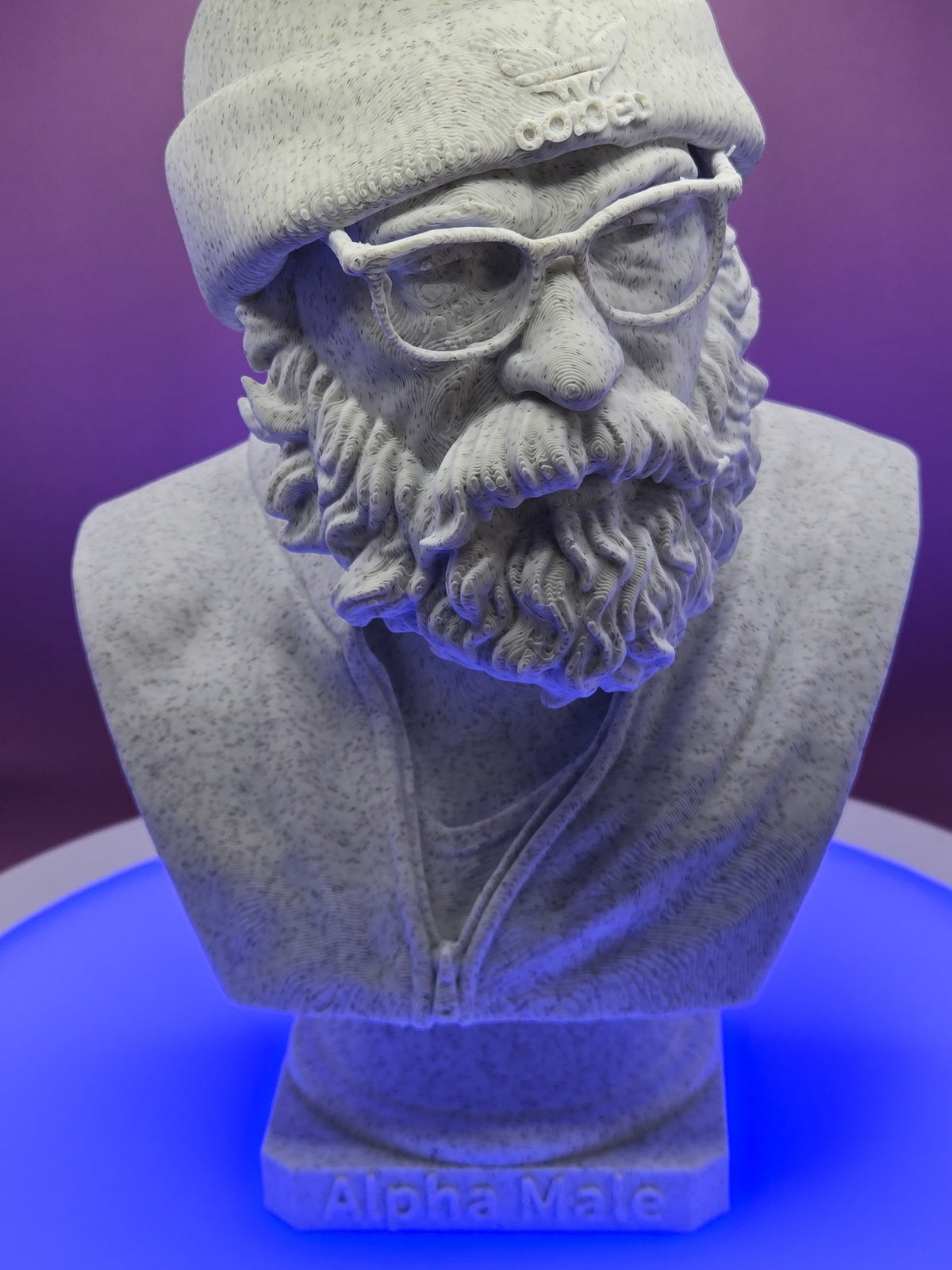 Alpha Male Bust by Mega Diamonds, real photo of the finished Marble PLA filament print, front view of the full bearded bust in a beanie, glasses and zip jacket on a plinth lettered Alpha Male